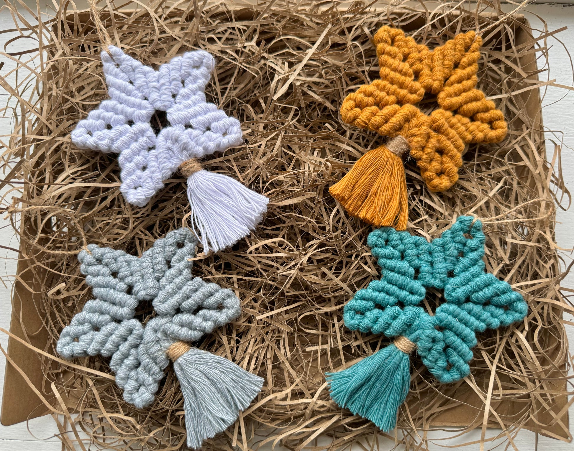 Four star-shaped decorative items with tassels on a bed of straw.