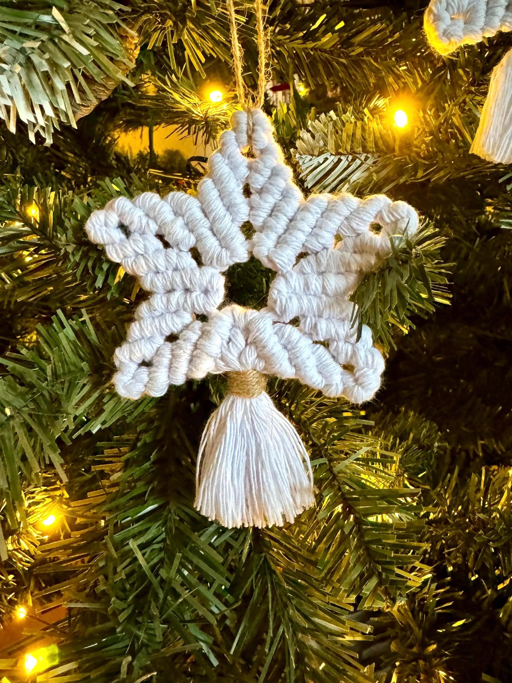 White macrame star ornament hanging on a Christmas tree with lights.
