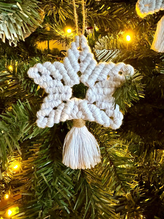 White macrame star ornament hanging on a Christmas tree with lights.