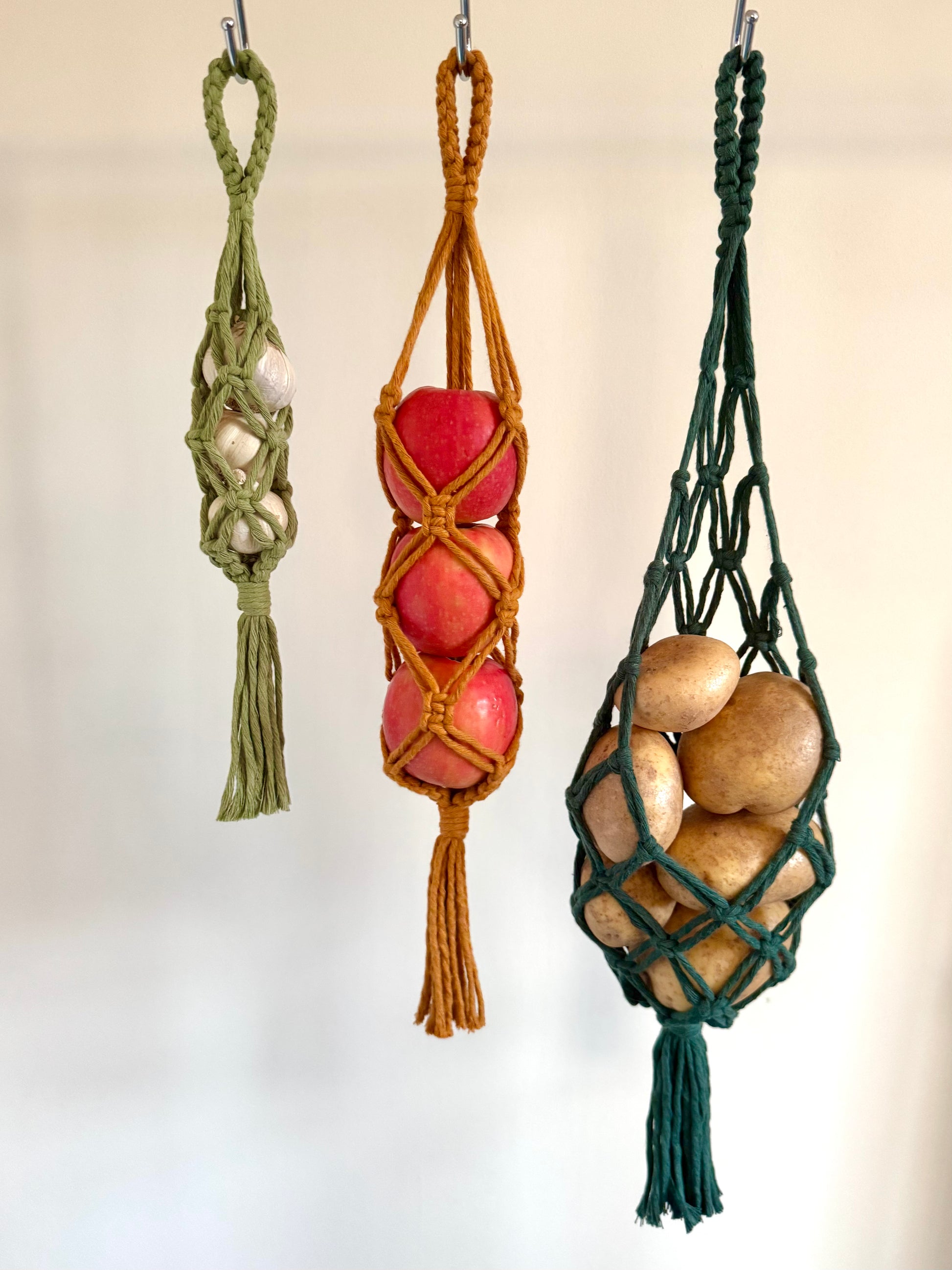 Three macrame nets in green, yellow , and dark green holding fruits and vegetables against a white background.