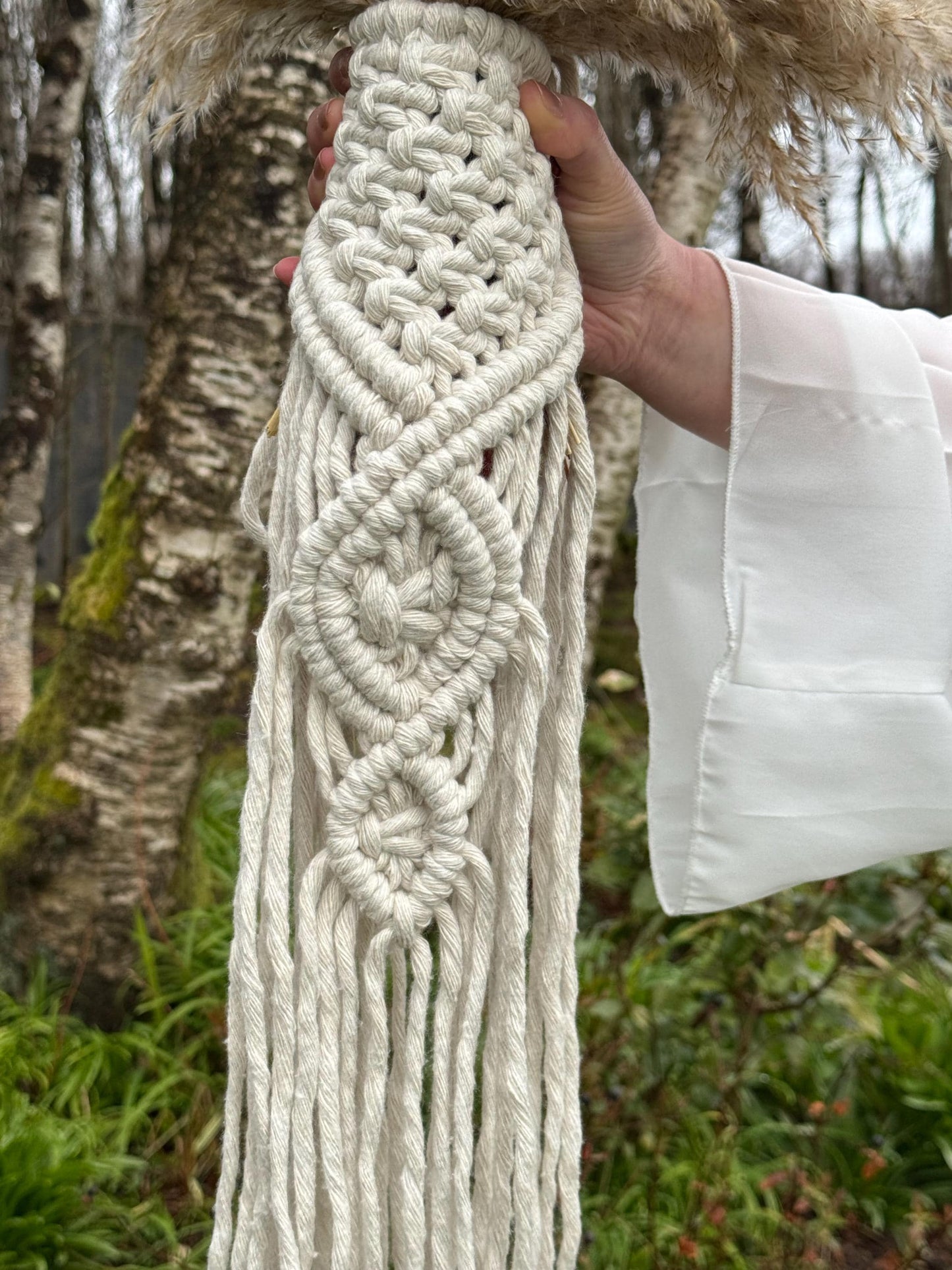 Close-up of a hand holding a macrame bouquet wrap / flowers holder tied around a pampas grass bouquet 