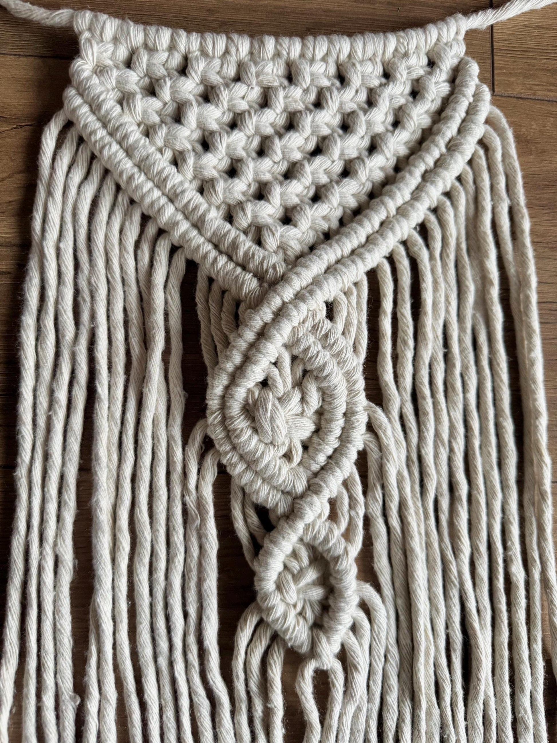 Close-up of a macrame wall hanging with intricate patterns on a wooden surface.