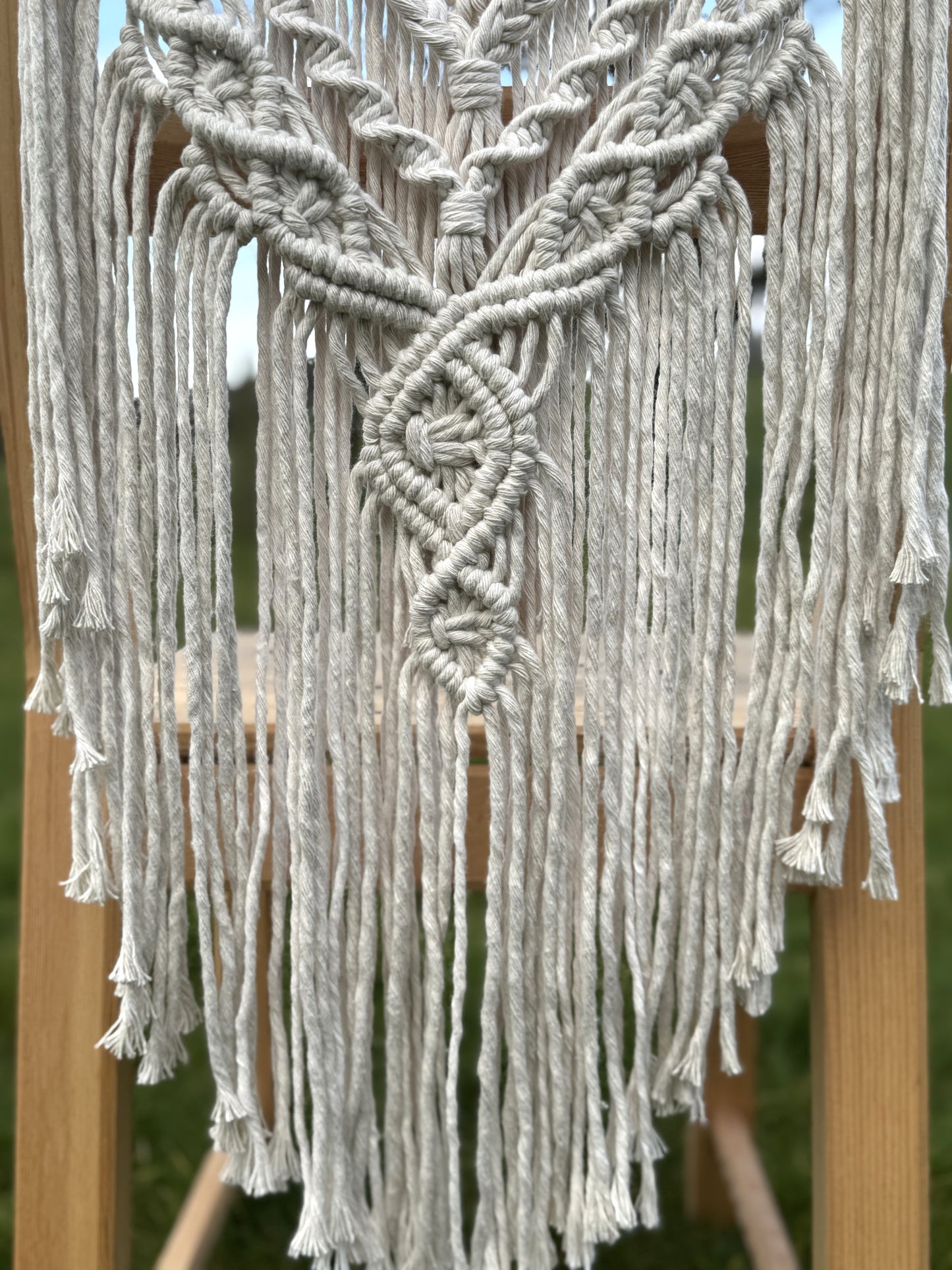 Macrame with intricate patterns and tassels on a wooden stand.