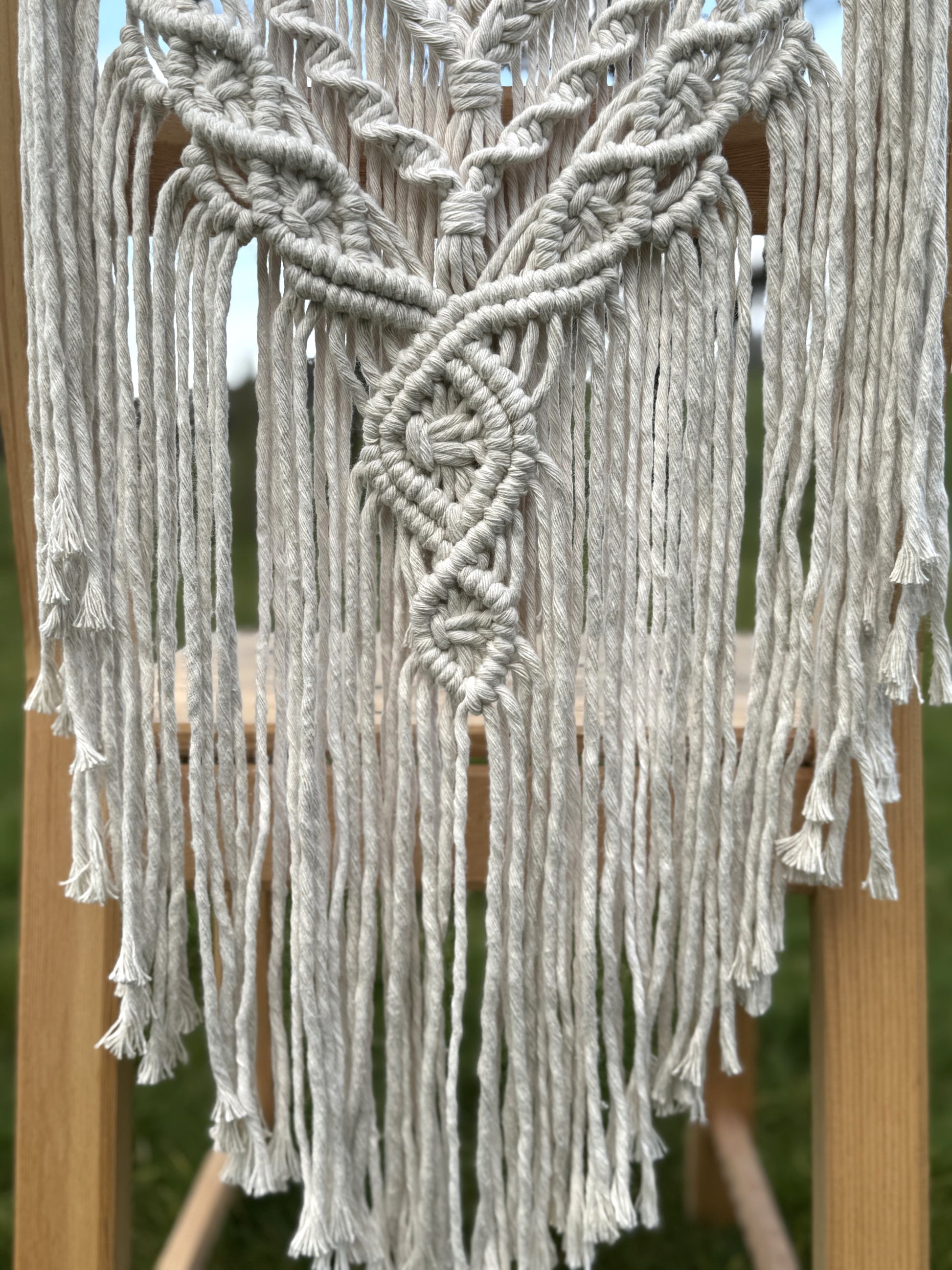 Macrame with intricate patterns and tassels on a wooden stand.