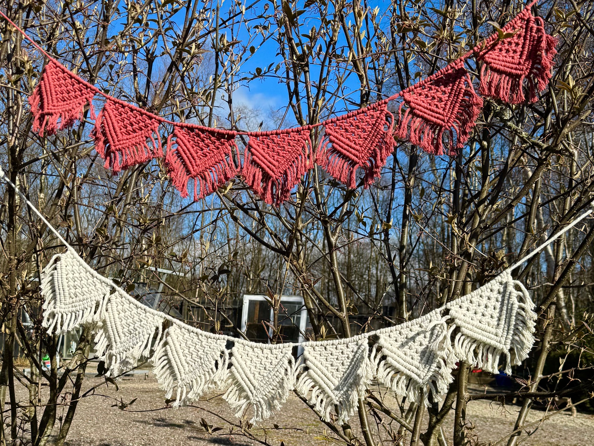 Macrame banners in terracotta and white hanging between trees against a blue sky.