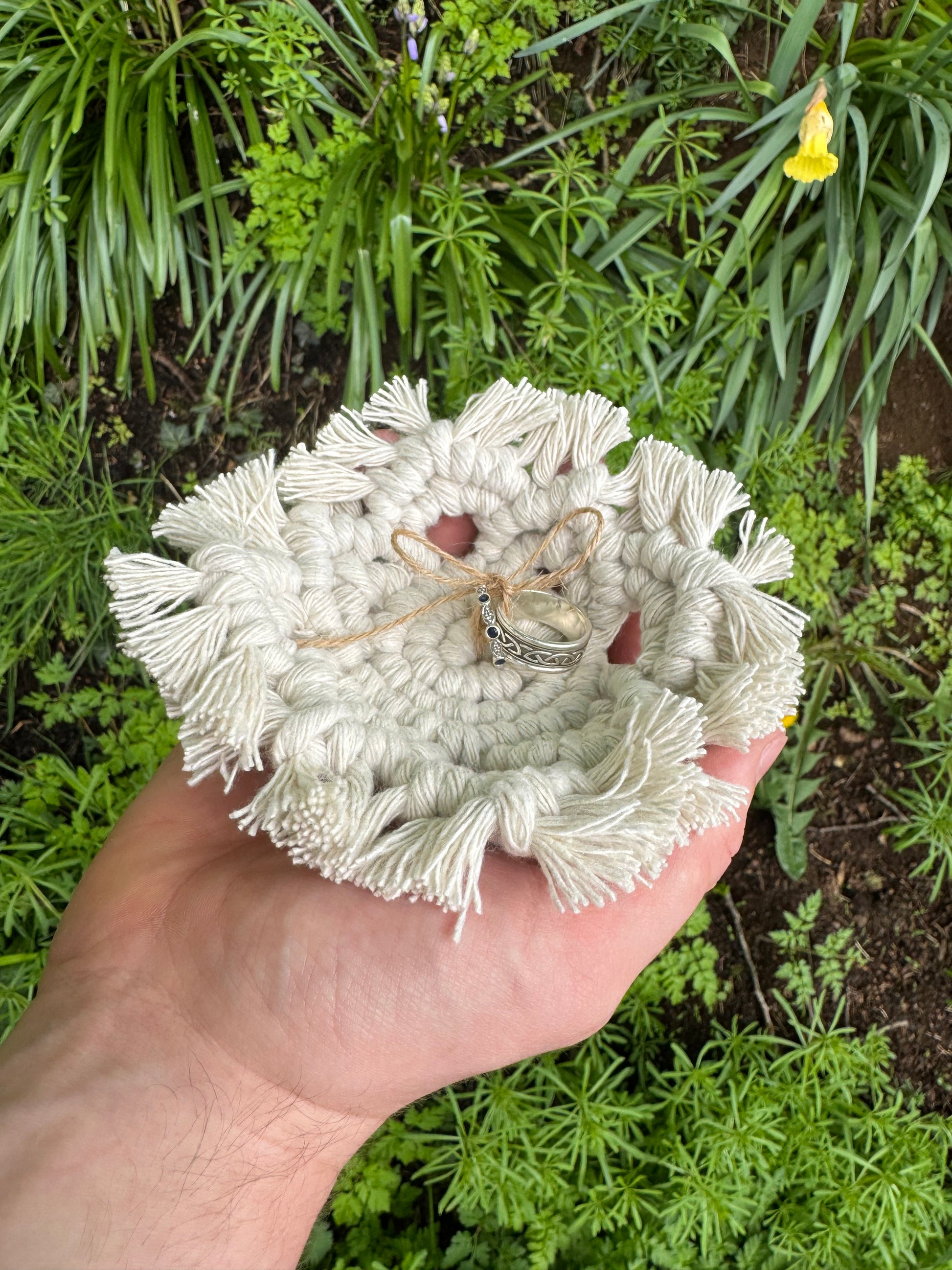 Hand holding a white textured dish with jewelry against a green plant background