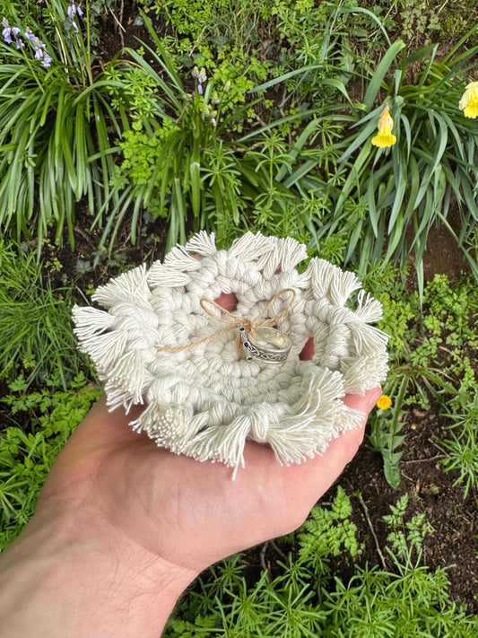 Hand holding a textured white macrame ring holder with plants in the background