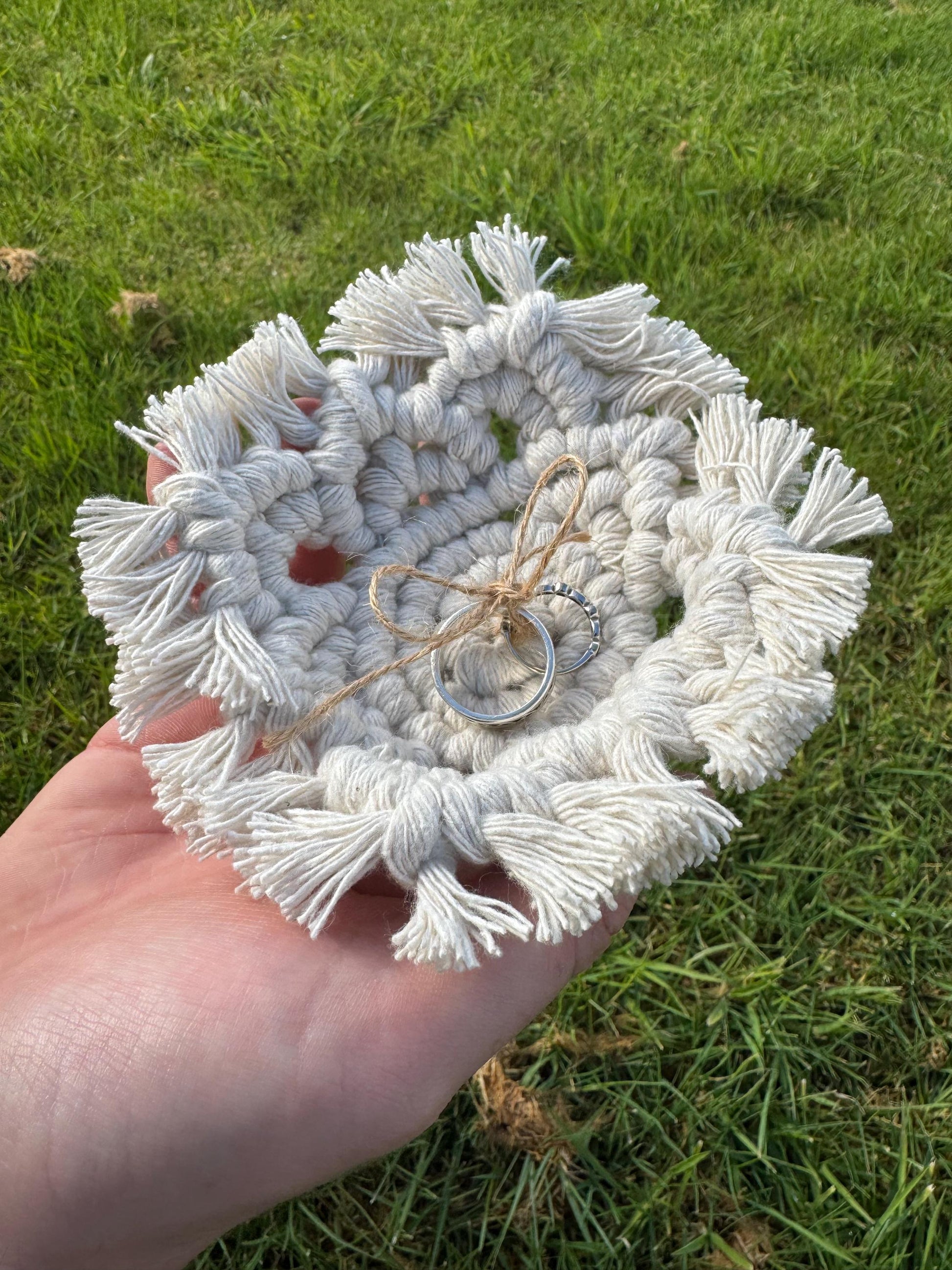 Hand holding a white macrame coaster with tassels on grass