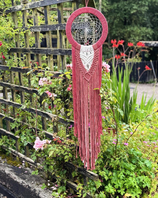 Red macrame wall hanging with a dreamcatcher design in a garden setting