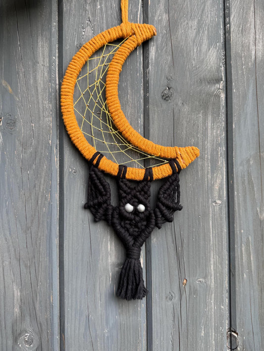 Halloween-themed dreamcatcher with black bat and yellow crescent moon design on a wooden background