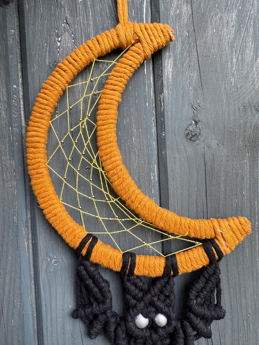 Orange and black dreamcatcher with batdesign on a wooden surface
