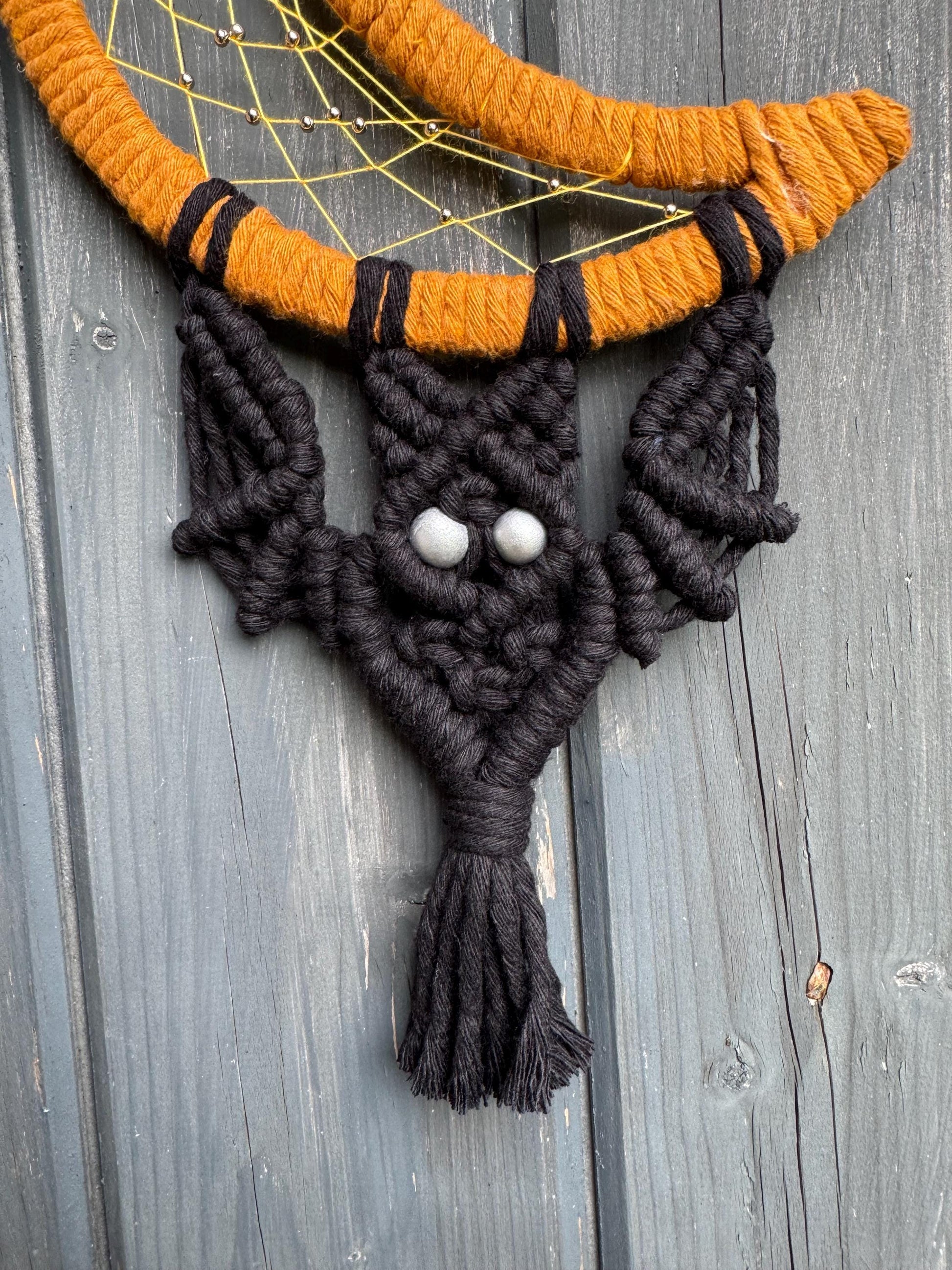 Macrame bat wall hanging with orange and black colors on a wooden surface