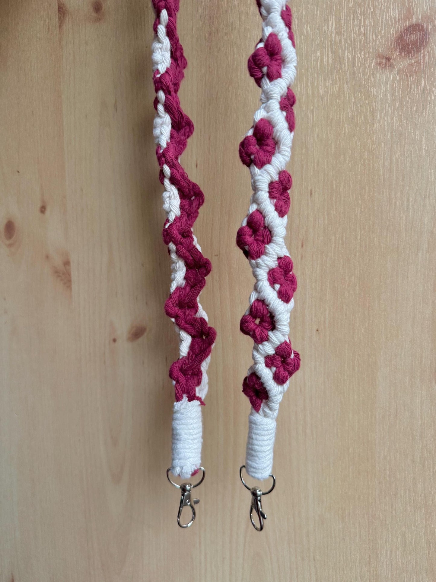 off-white macrame strap with burgundy flower detailing against a wooden background