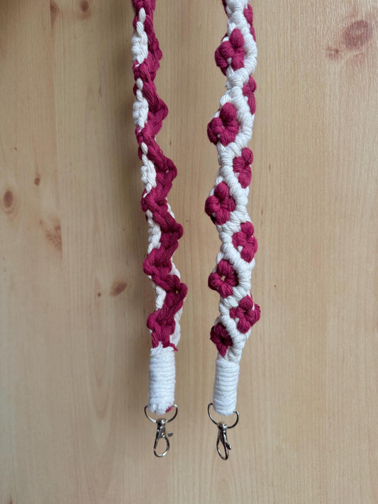 off-white macrame strap with burgundy flower detailing against a wooden background