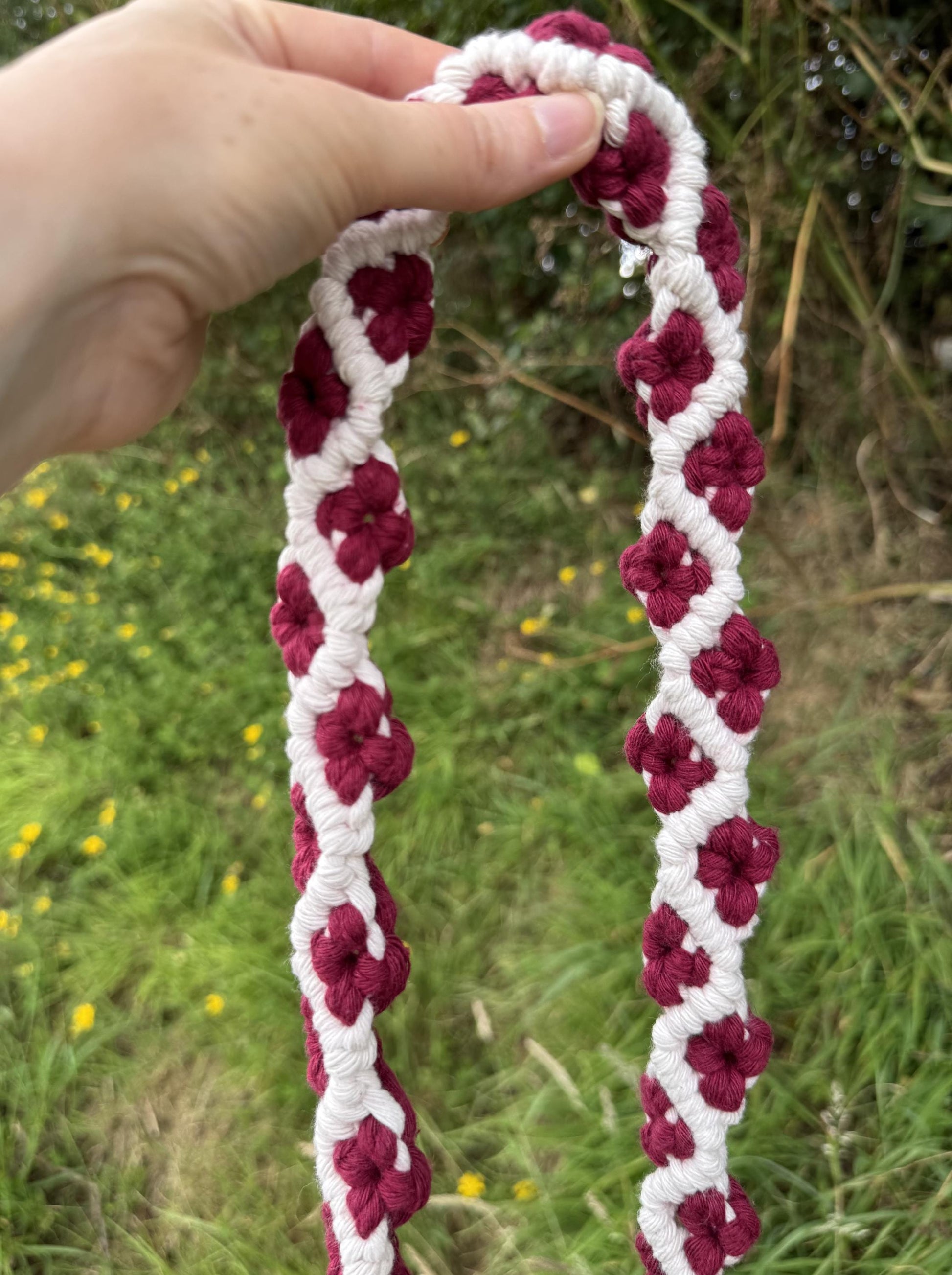 Hand holding a macrame white and red floral strap against a natural background