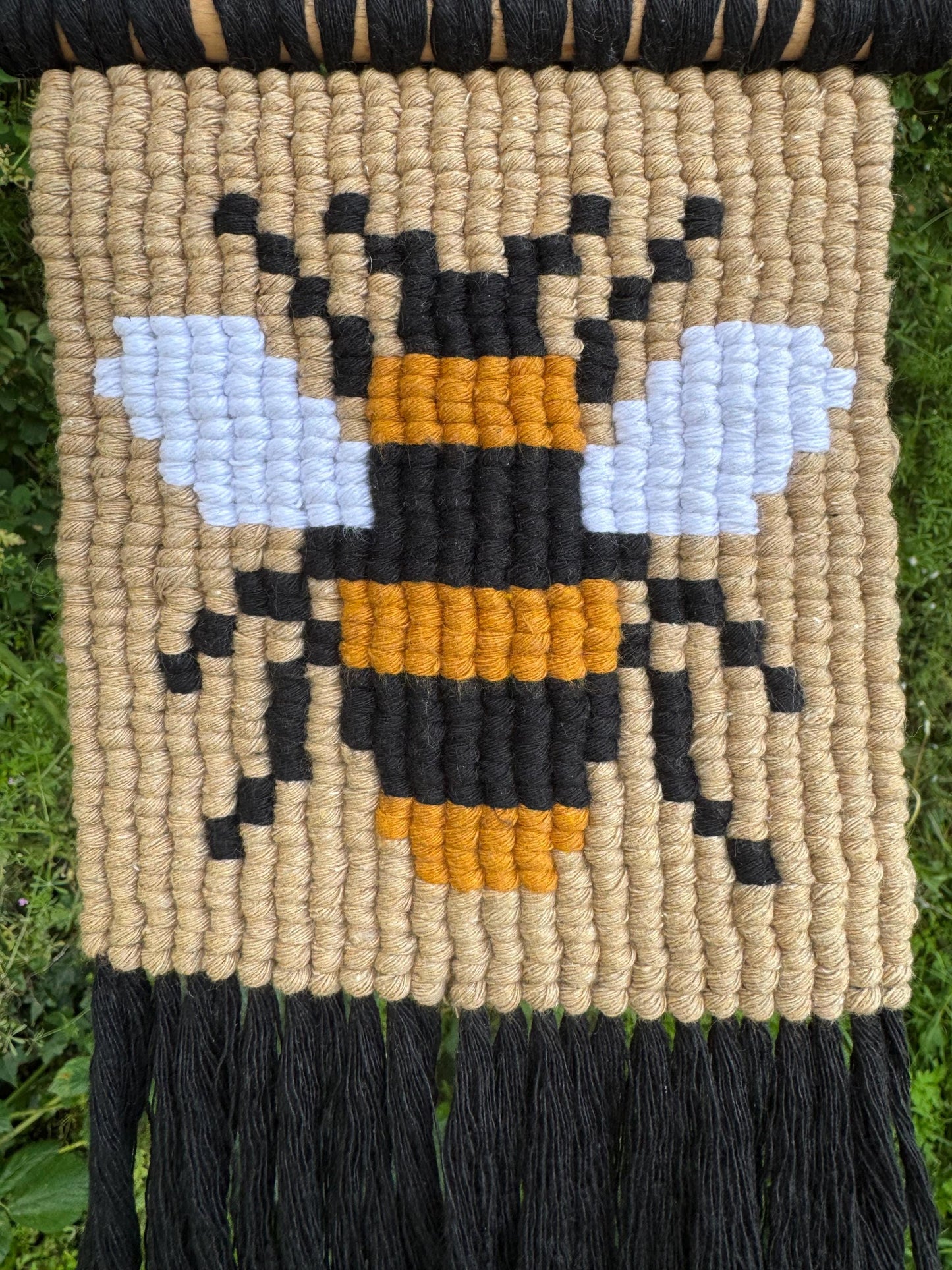 Woven wall art with a bee design on a natural fiber background