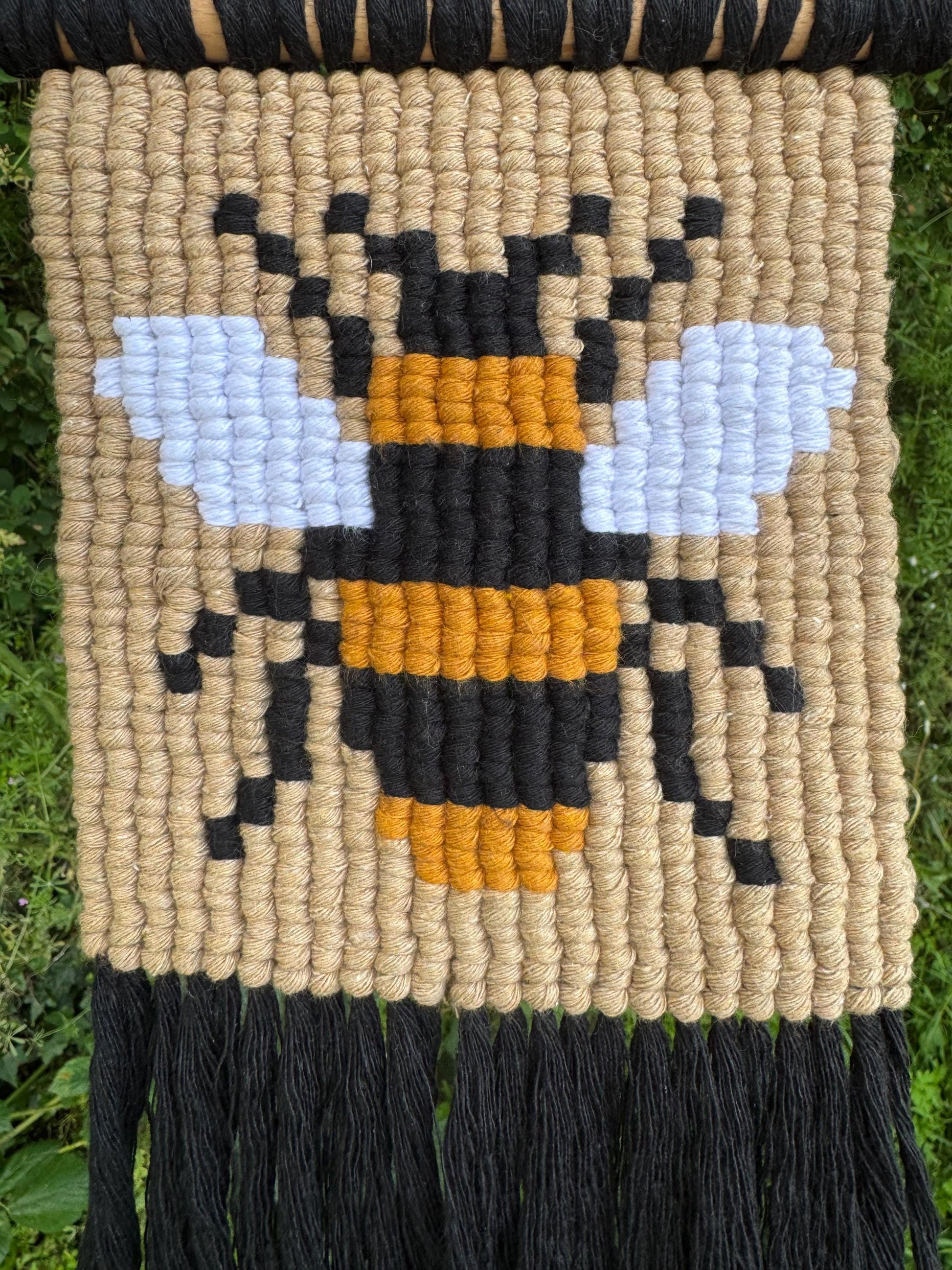 Woven wall art with a bee design on a natural fiber background