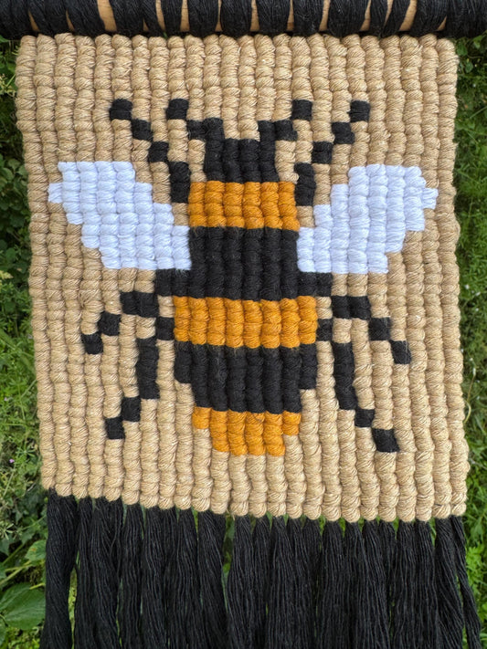 Woven wall art with a bee design on a natural fiber background