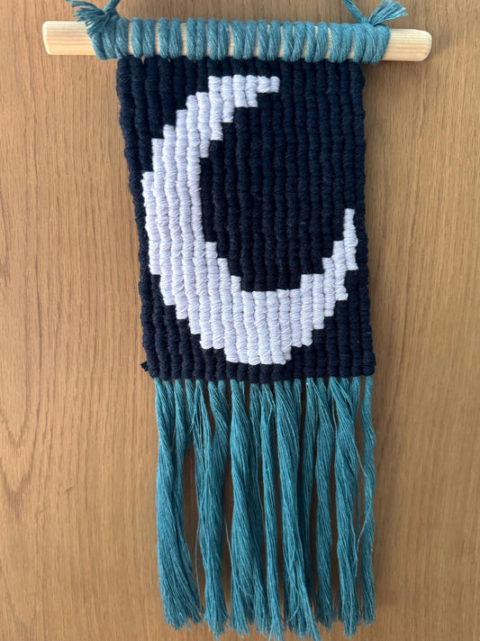 Macrame wall hanging with a moon design on a wooden surface
