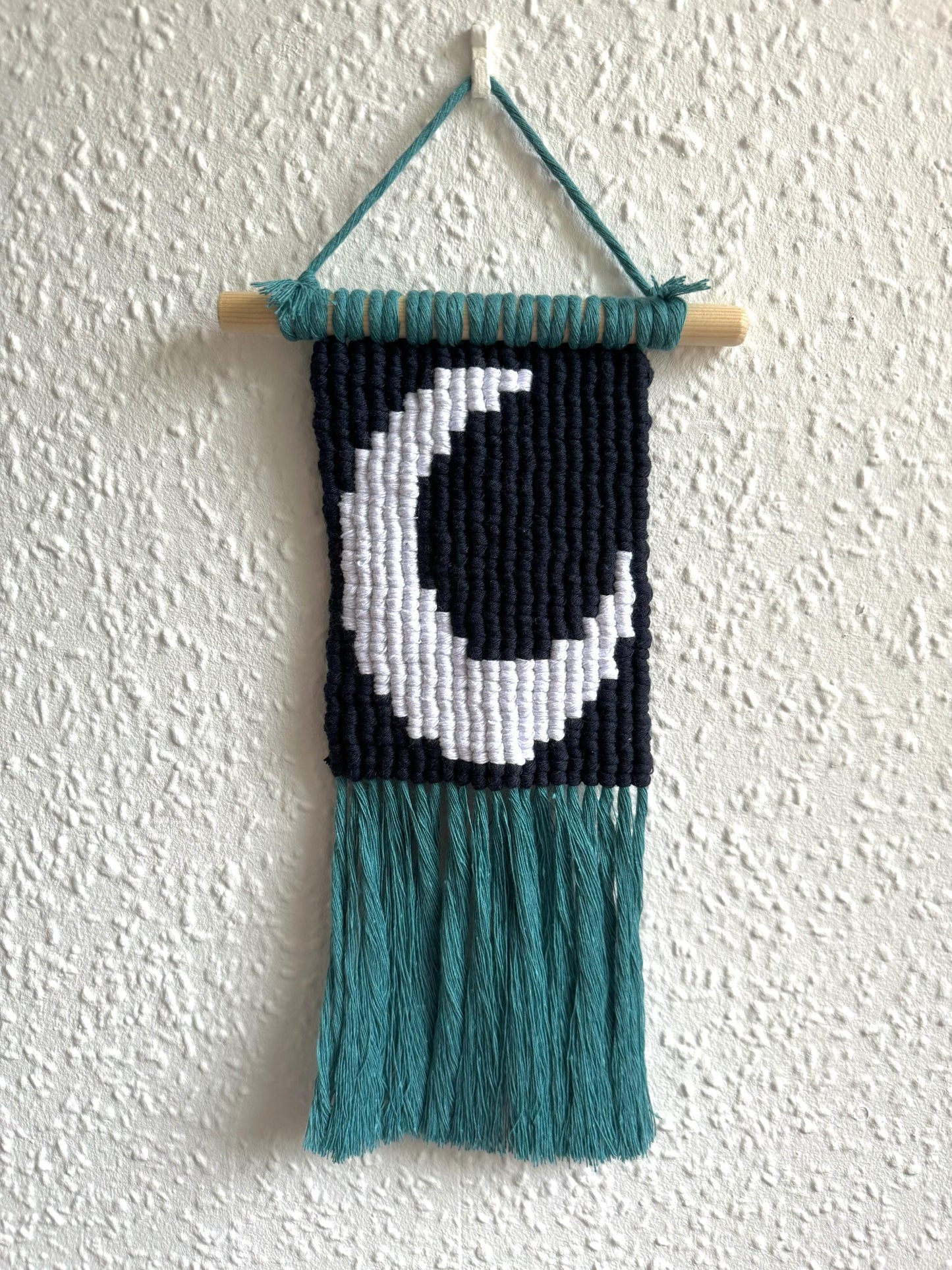 Macrame wall hanging with a pixel moon design on a textured white wall