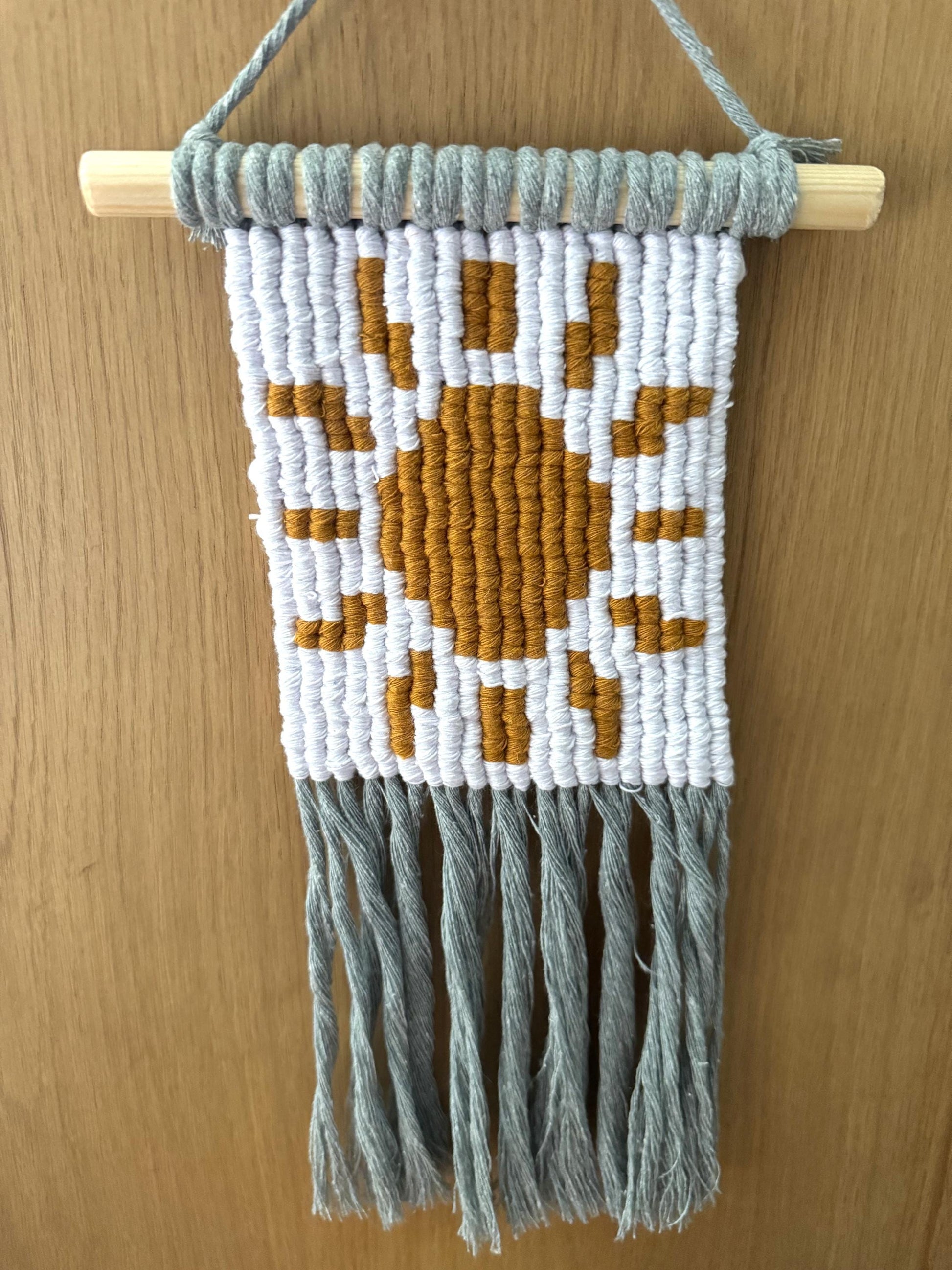 Macrame wall hanging with pixel sun design on a wooden surface