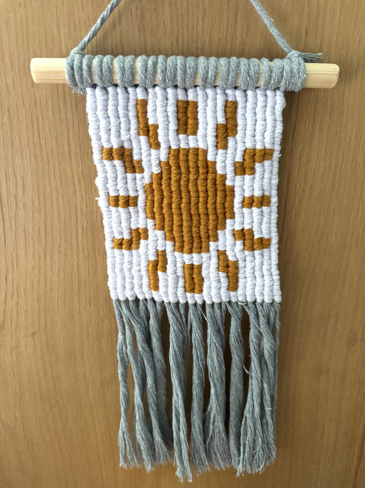 Macrame wall hanging with pixel sun design on a wooden surface