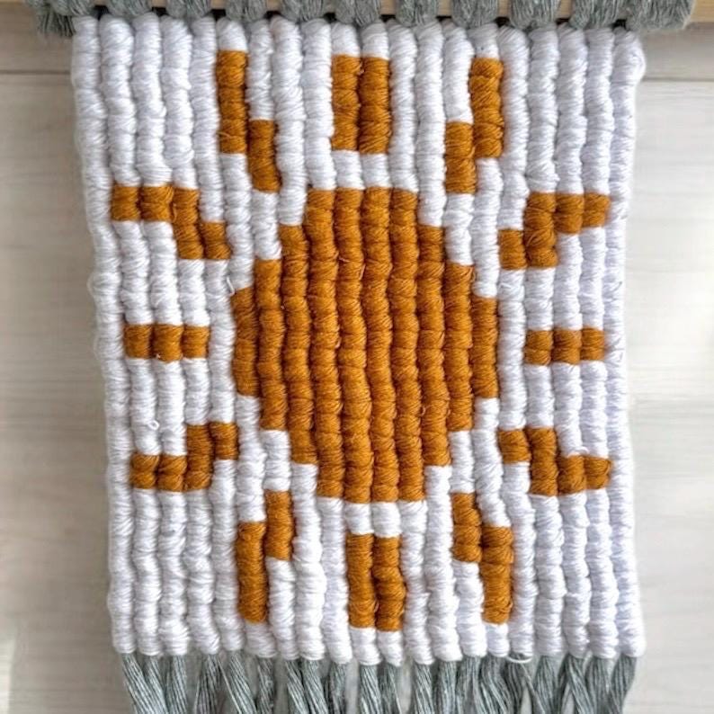 Macrame wall art with a pixelated sun pattern in white, yellow and grey