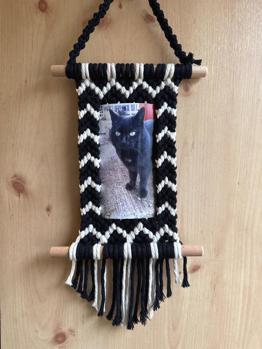 Black and white zig zag macrame photo frame with a photo of a black cat on a wooden surface