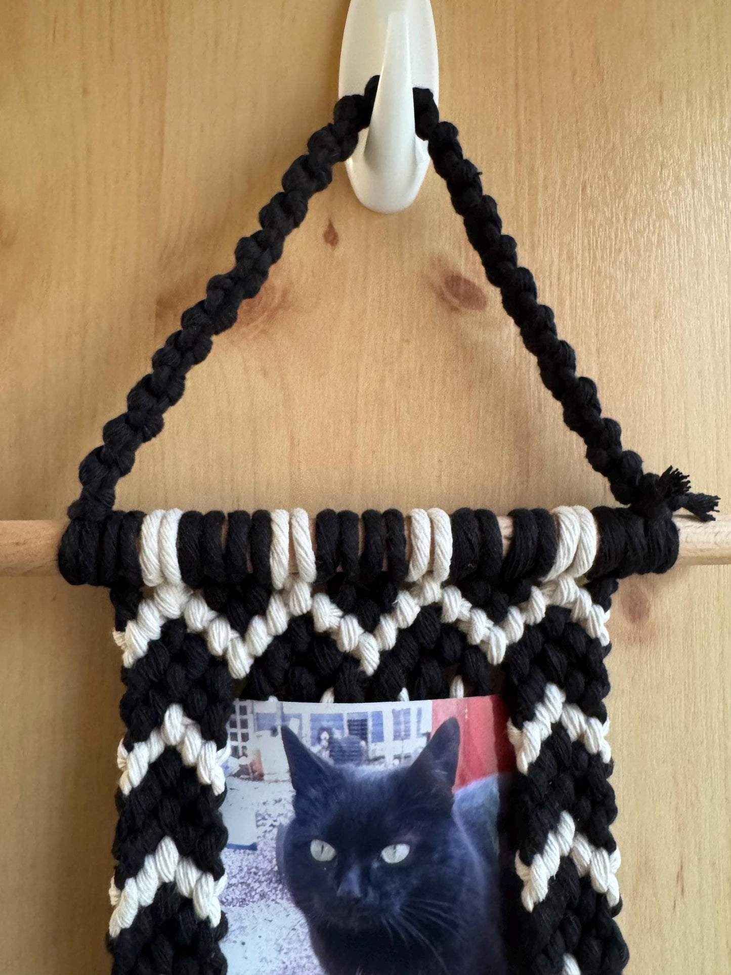 Black and white woven wall hanging with a cat photo on a wooden surface