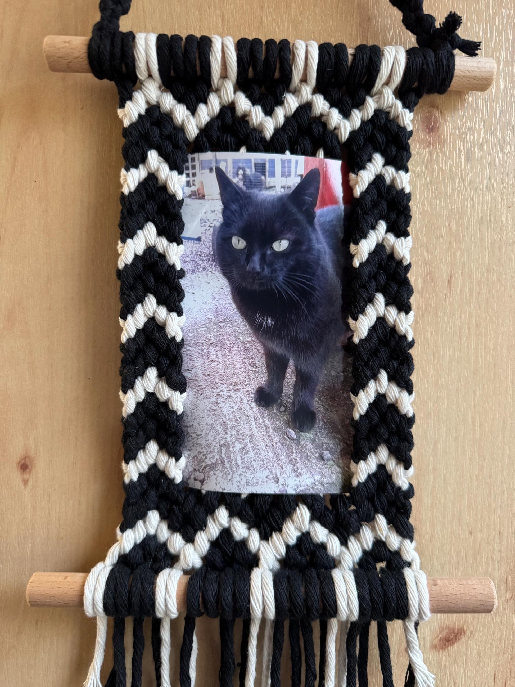 Black and white woven wall hanging with a cat photo inside on a wooden surface