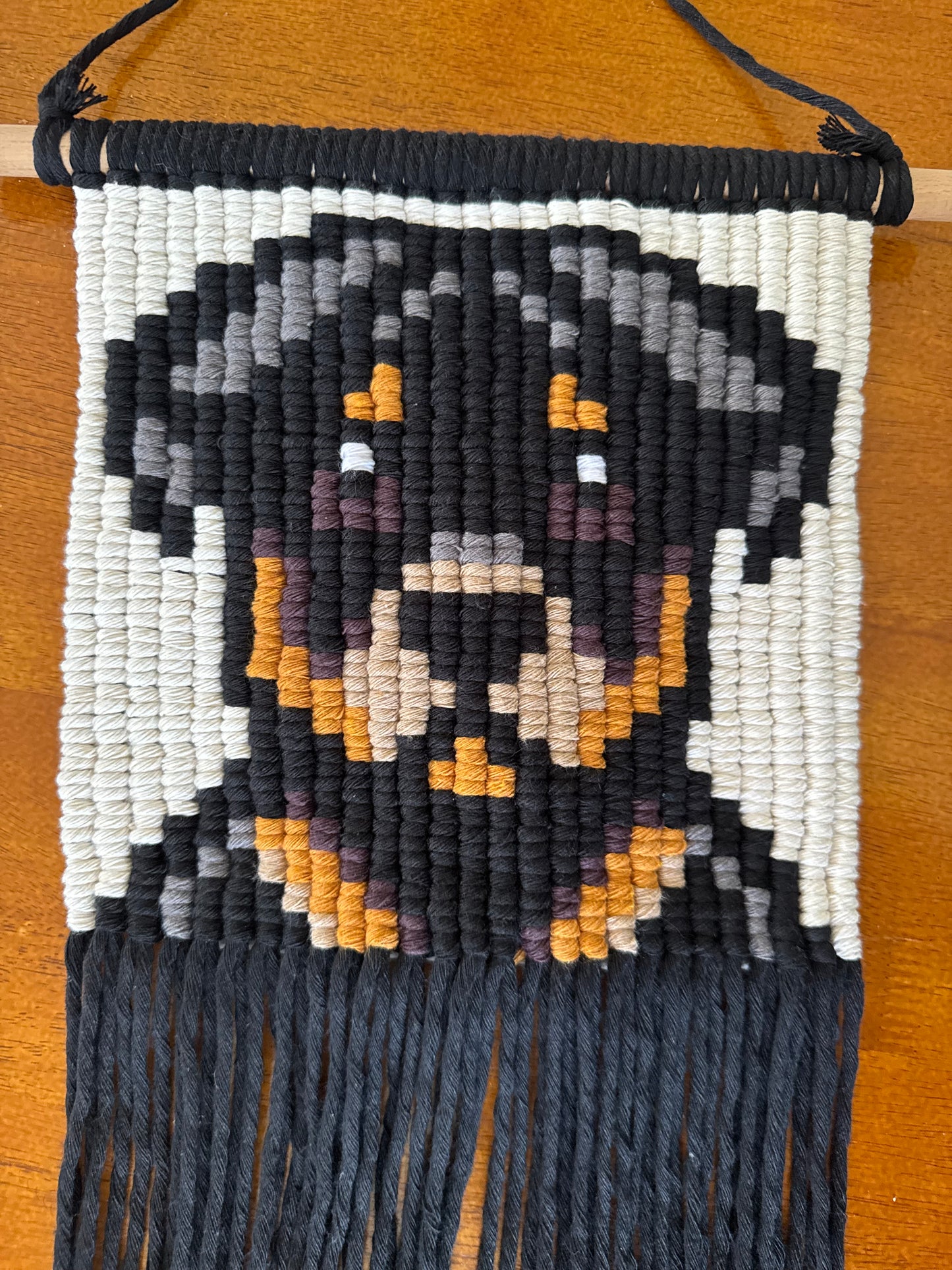 Woven tapestry of a dog with black, white, and orange colors on a wooden surface.