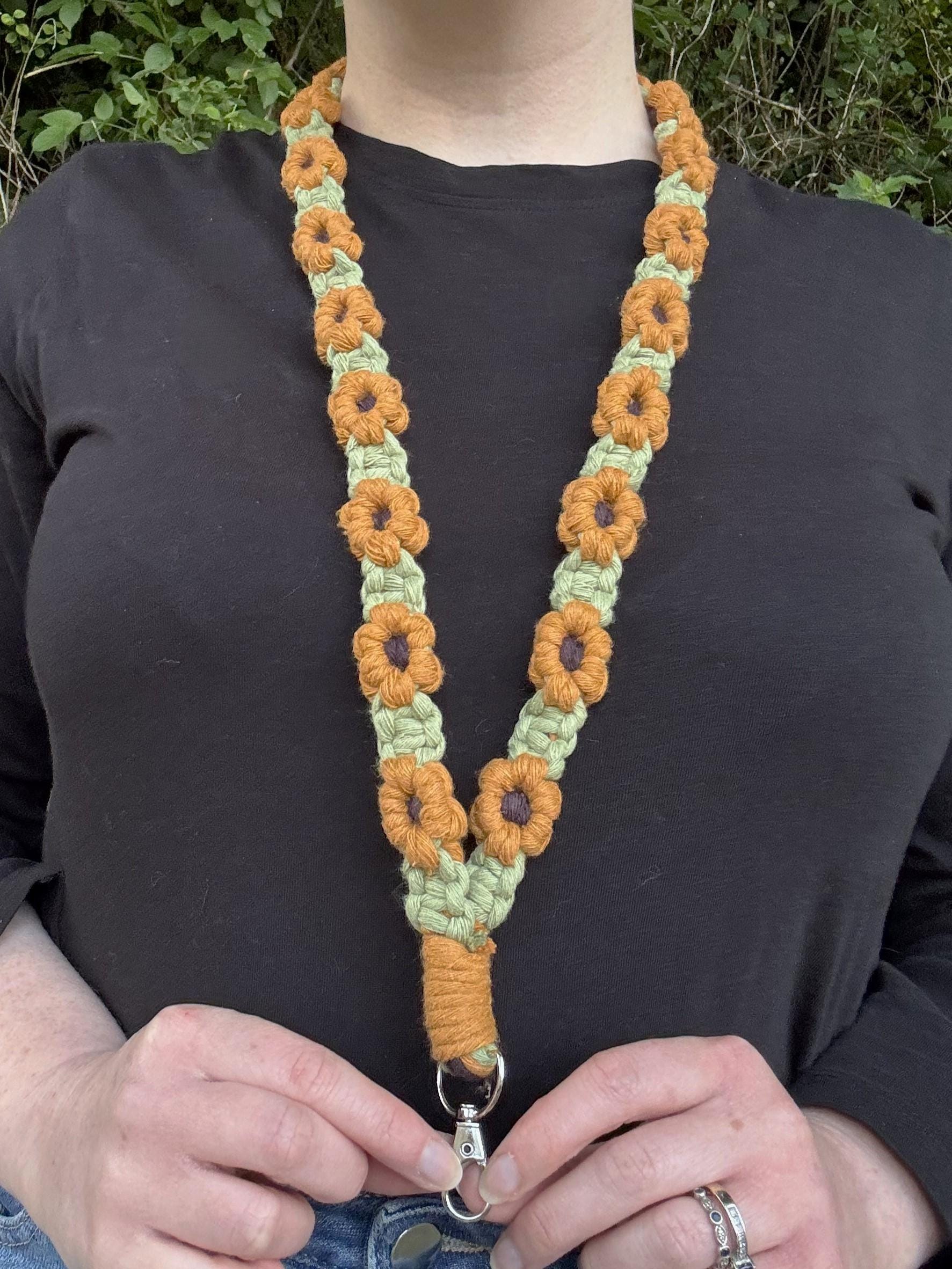 Person wearing a colorful macrame lanyard with floral patterns against a natural background.