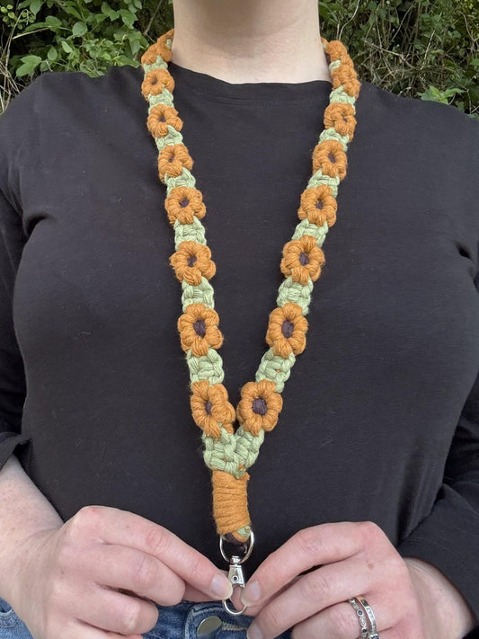 Person wearing a colorful macrame lanyard with floral patterns against a natural background.