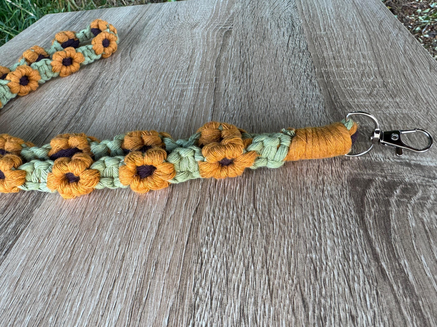 Green handmade macrame lanyard with sunflower designs on a wooden surface