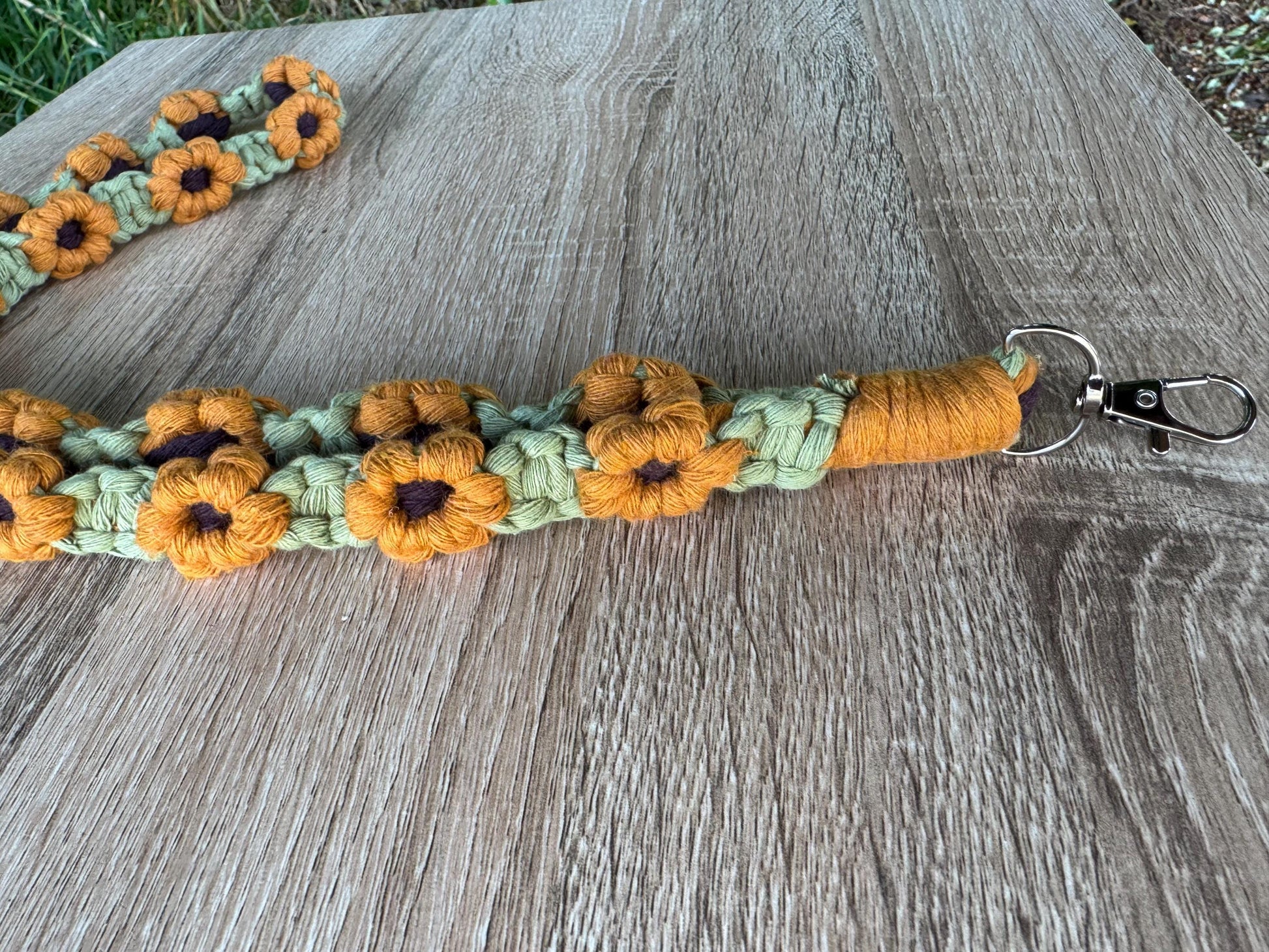 Green handmade macrame lanyard with sunflower designs on a wooden surface
