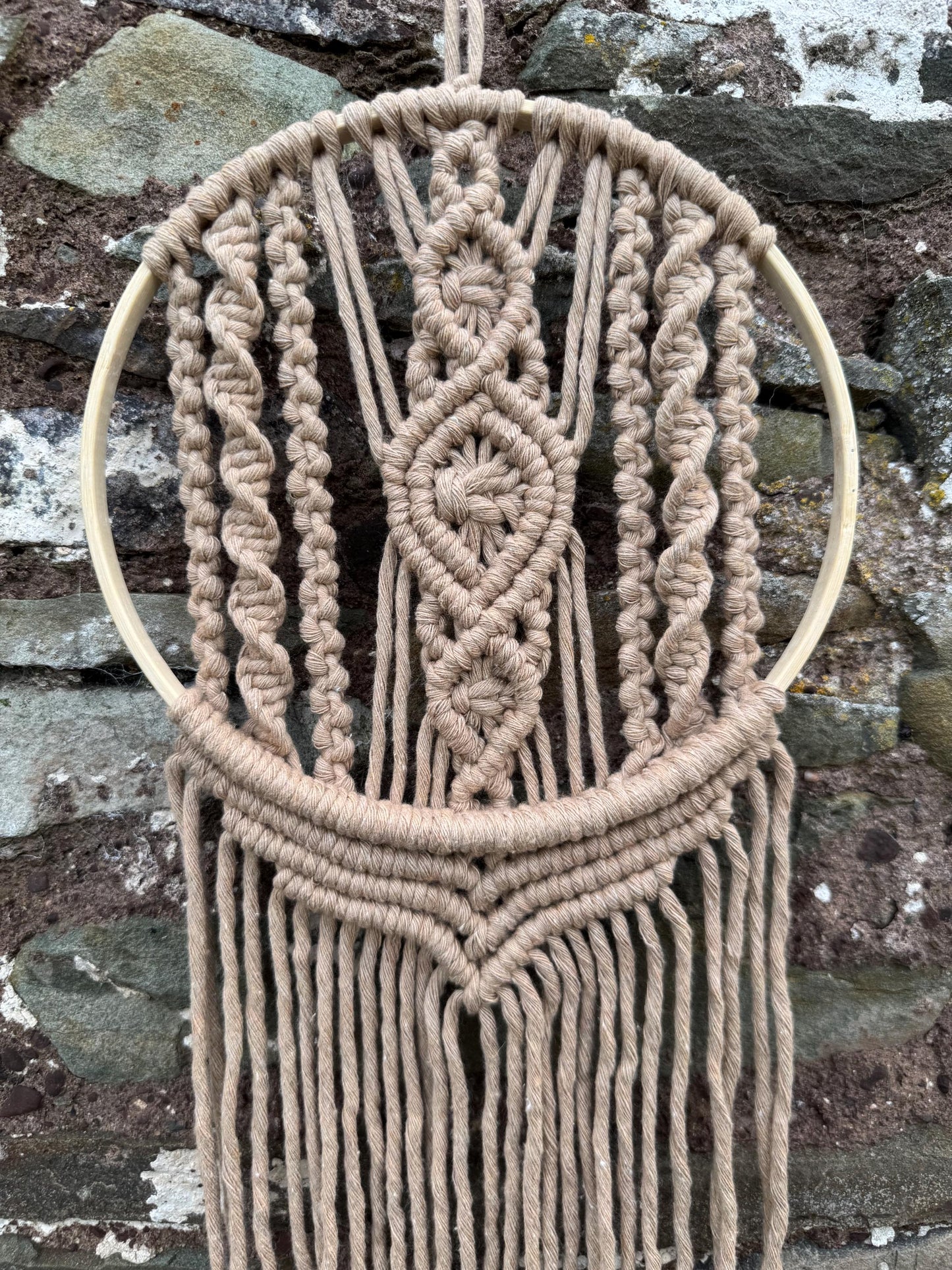 Macrame wall hanging with geometric pattern against a stone wall background