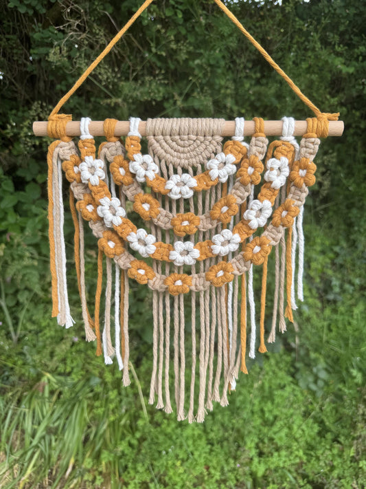 Macrame wall hanging with floral patterns against a green natural background