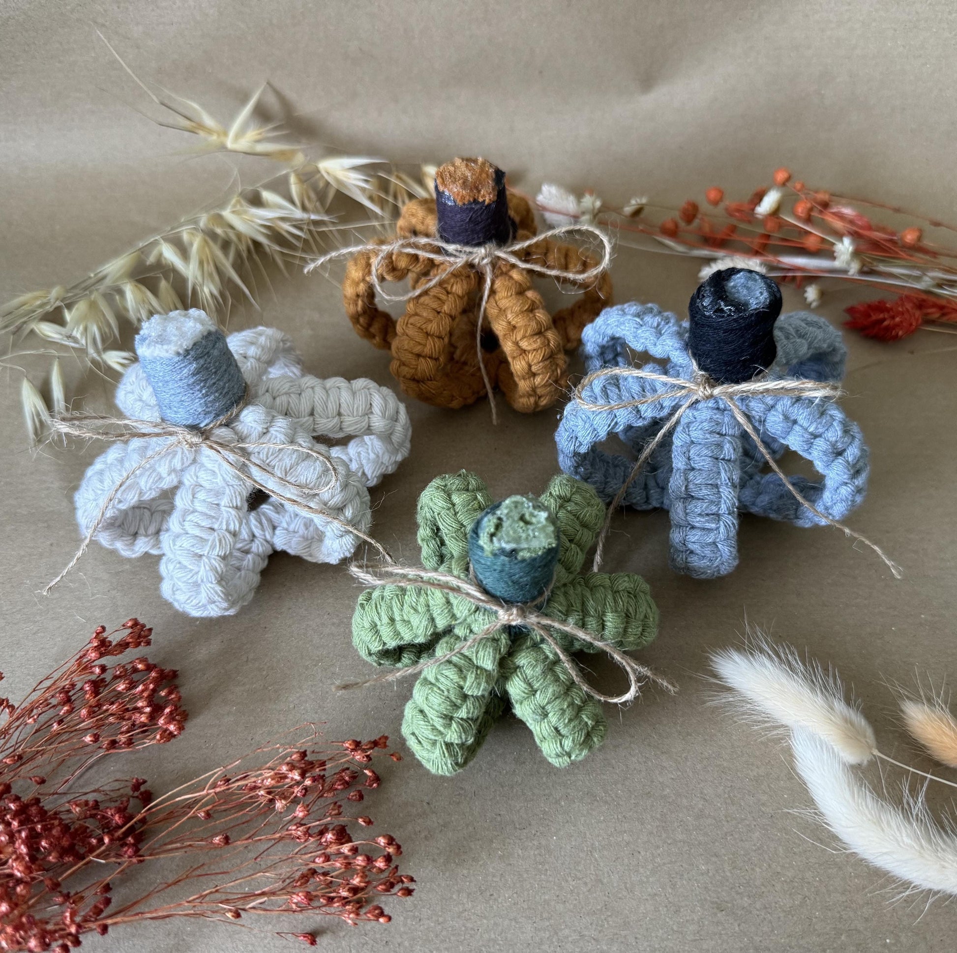 Set of macrame decorative pumpkins in various colors on a neutral background with dried flowers and feathers.