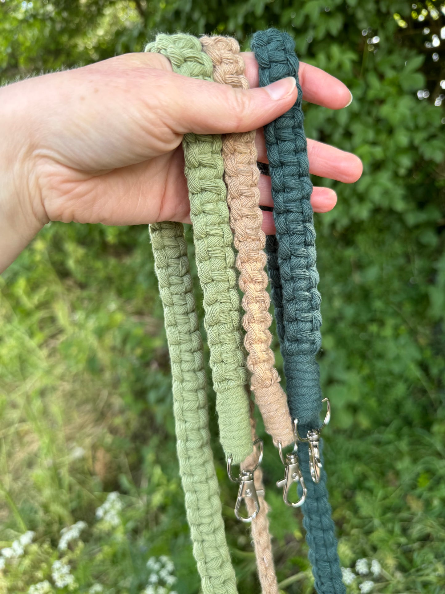 Hand holding three macrame bag straps of different colours against a natural background.