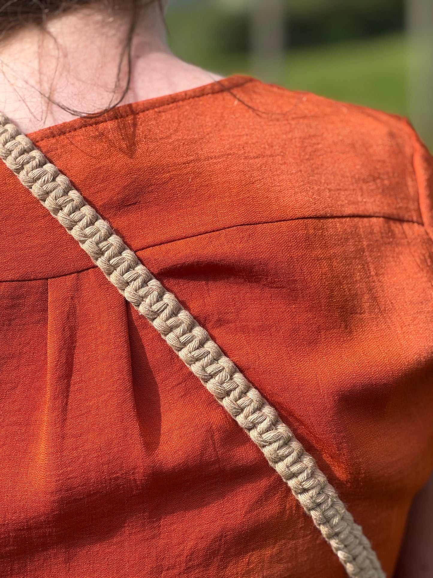 Close-up of a person wearing an orange garment with a beige strap over shoulder outdoors.