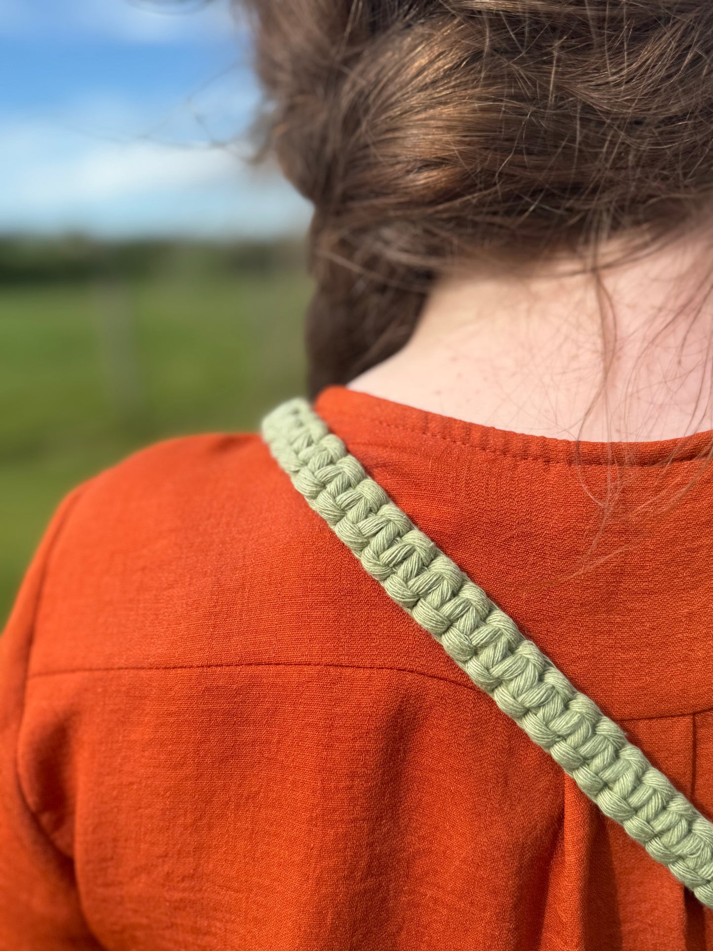 Person wearing an orange shirt with a green strap over shoulder, blurred natural background