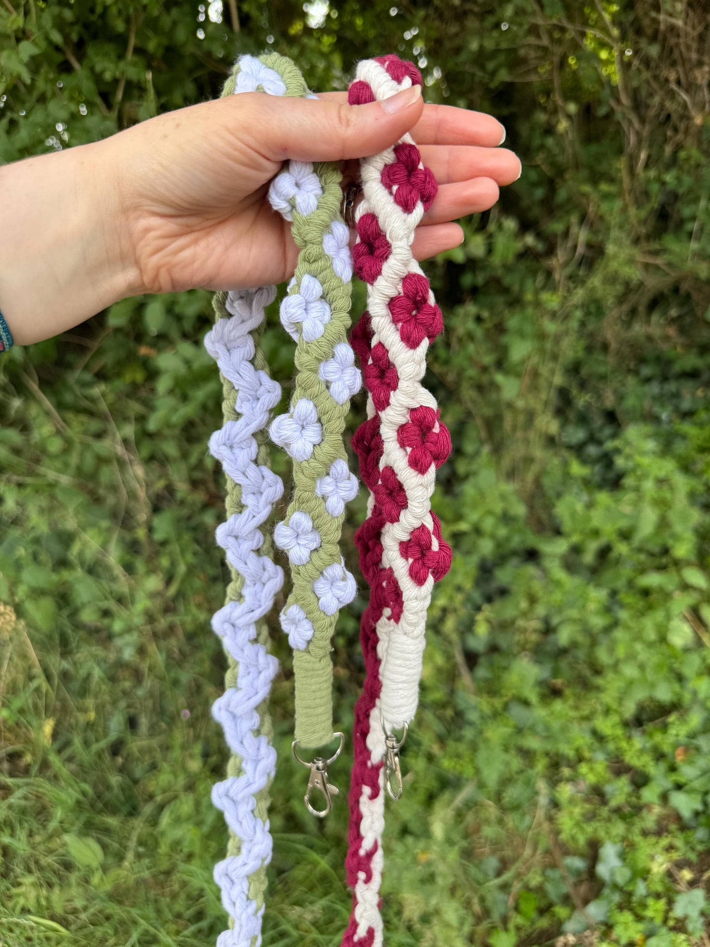 Hand holding two colourful floral straps against a natural background