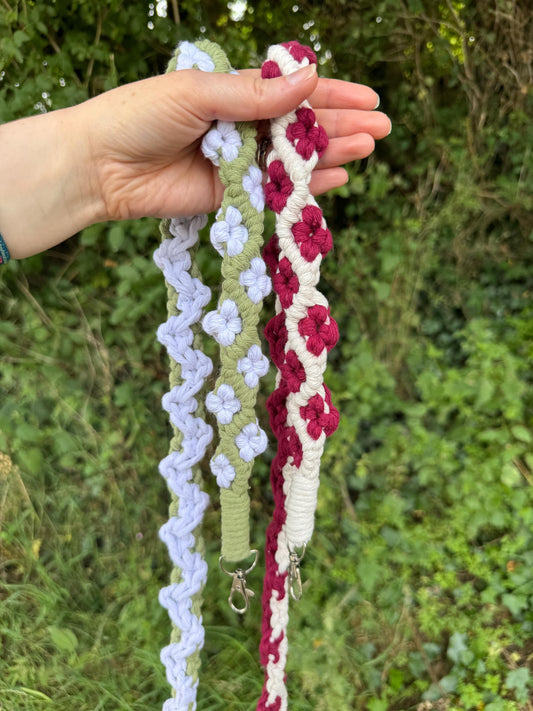 Hand holding two colourful floral straps against a natural background