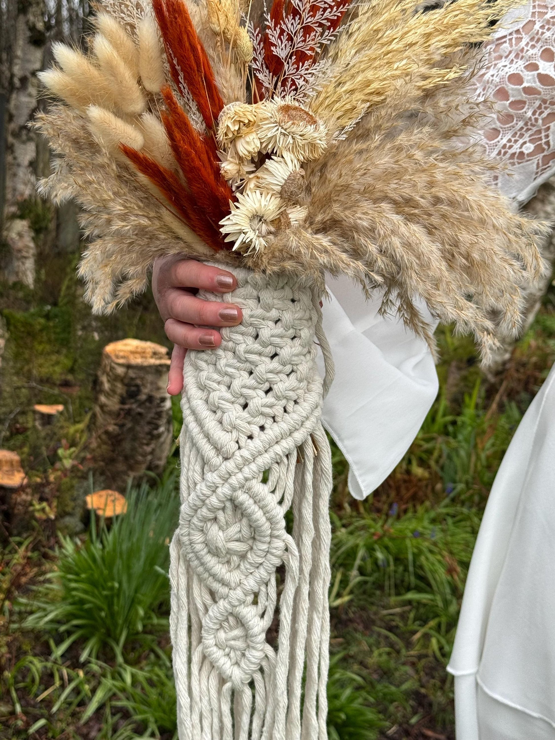 Hand holding a macrame bouquet wrap with dried flowers against a natural background