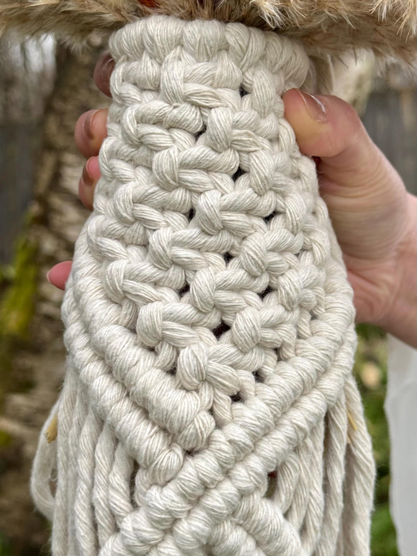 Close-up of a hand holding a knotted macrame beige rope against a blurred natural background