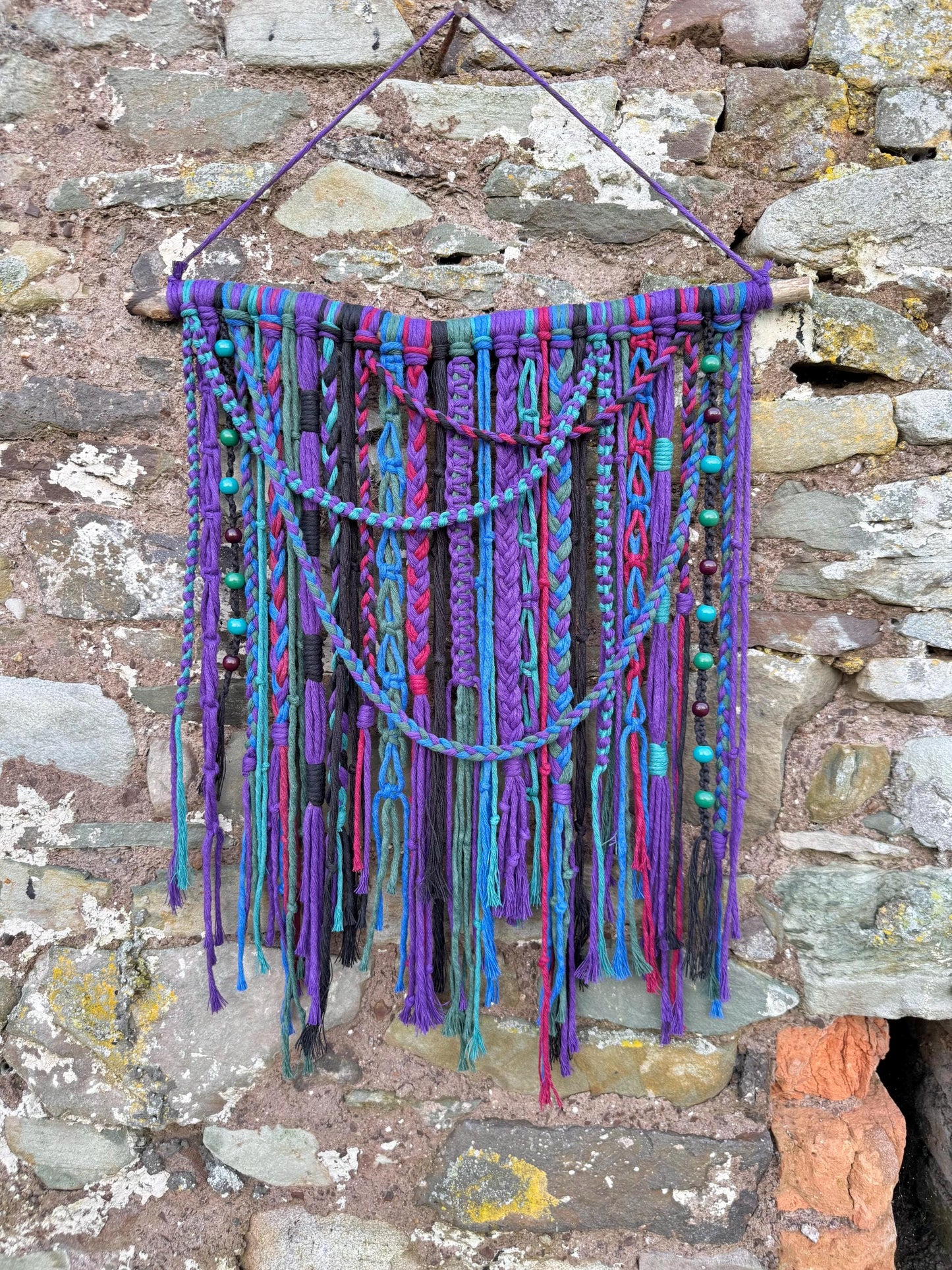 Colorful macrame wall hanging against a stone wall