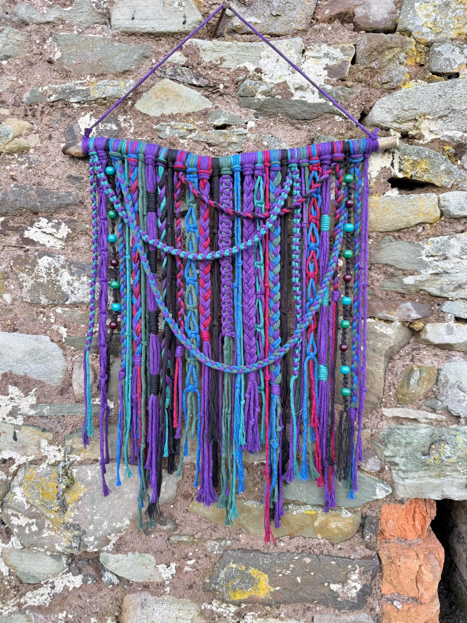 Colorful macrame wall hanging against a stone wall