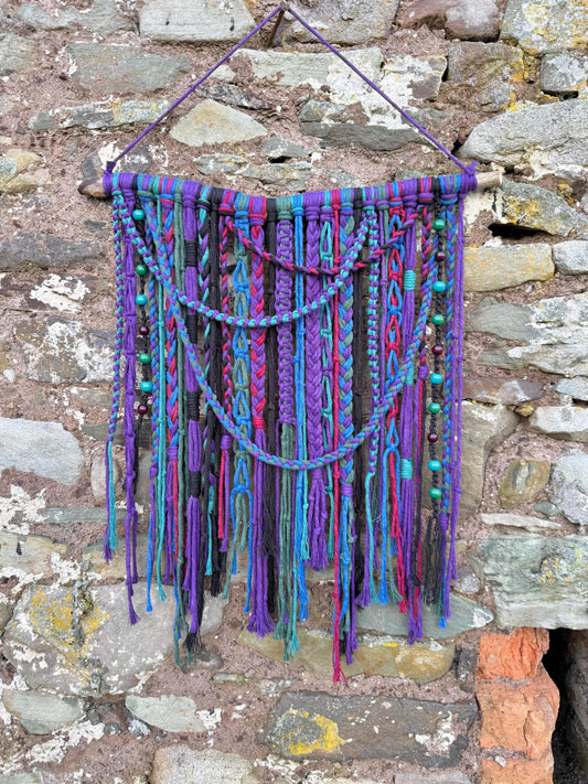 Colorful macrame wall hanging against a stone wall