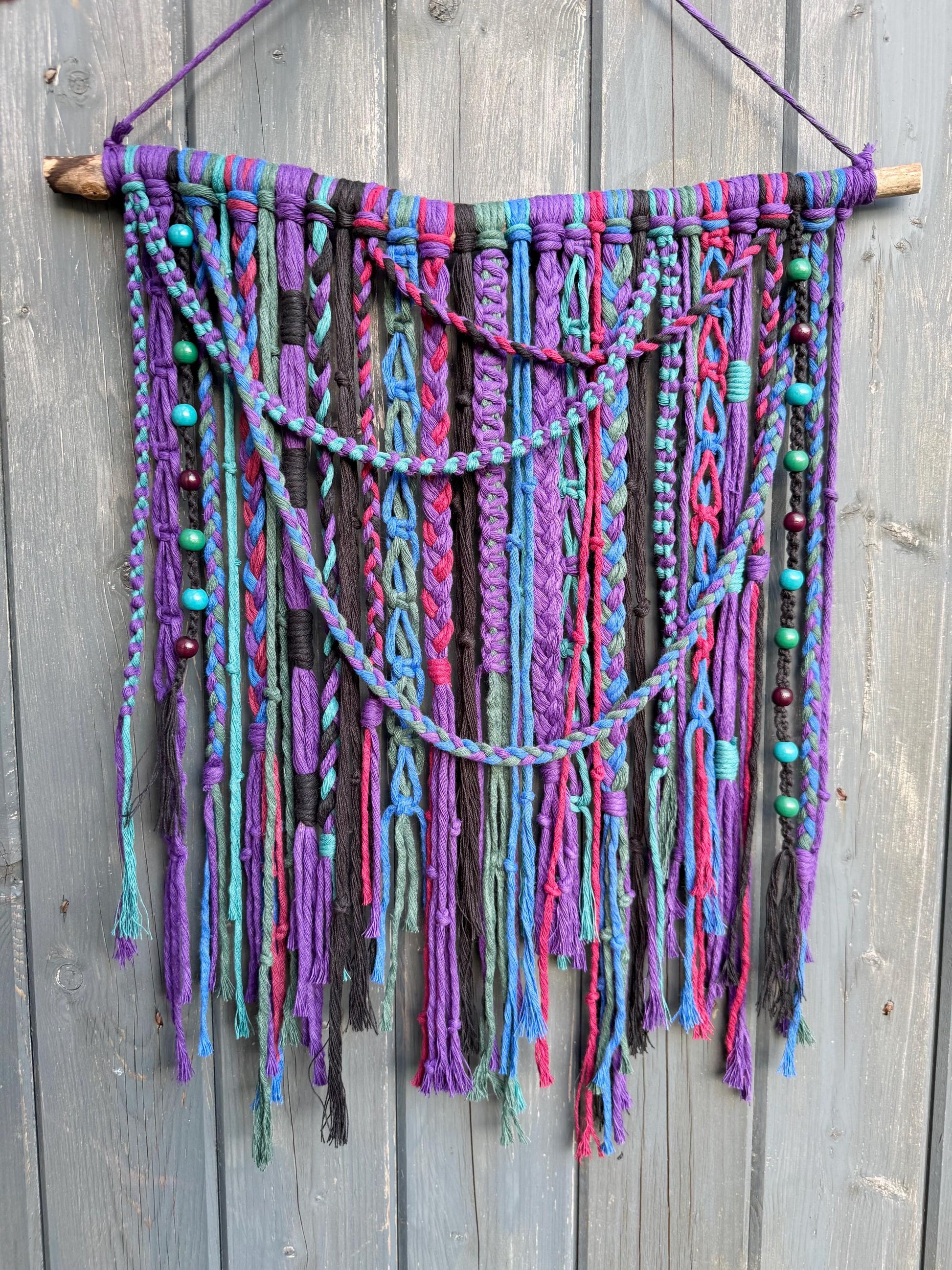 Colorful knotted wall hanging with beads on a wooden background